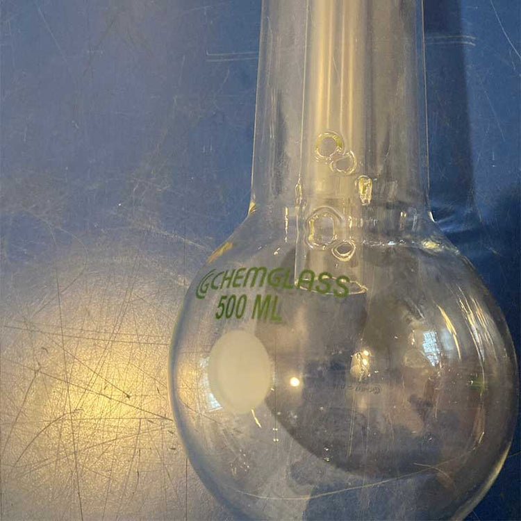 Clear glass volumetric flask with 'GChemglass 500 mL' label on a blue surface